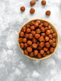 Hazelnut with peeled hazelnuts in small plate on concrete backgr